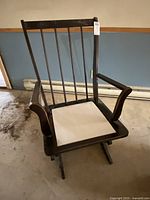Frontal view of wooden rocking chair showing vertical slats and missing seat cushion.
