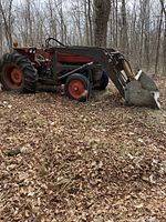 Overall side view of tractor in wooded area showing loader attached