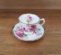 Teacup and saucer set with pink rose floral pattern and gold rim on wooden surface