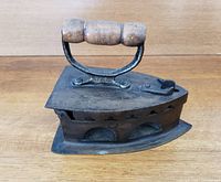 Side profile of the antique coal iron showing wooden handle, triangular base and ventilation slots.