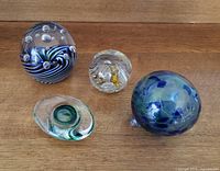 Overview of all four pieces including three paperweights and one blown glass ornament on wooden surface.
