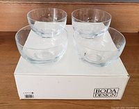Four clear crystal dessert bowls displayed on their original Boda Design box on a wooden surface.