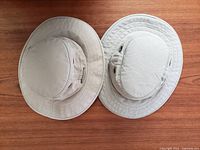 Top view of two light beige Tilley hats placed side by side on a wooden surface to show their overall condition and size difference.
