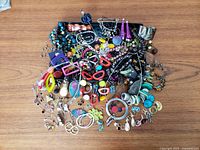 Top overview of entire jewelry lot spread on a tabletop showing various necklaces, bracelets, earrings, brooches and watches in mixed styles and colors