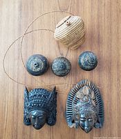 Overview photo of three small woven lidded baskets, woven bag with strap, and two wooden carved masks displayed on wooden surface