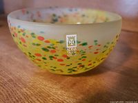 Close-up side view of the round frosted yellow bowl with multi-colored speckles and Mdina Glass Malta label on the side
