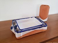 Two terracotta rectangular baking forms stacked, showing terracotta body with blue rims and decorative handles