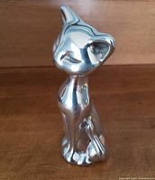 Front view of polished cast aluminum cat sculpture showing smooth reflective surface and stylized details.