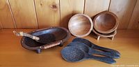 Four coconut shell serving spoons, three small wooden kava bowls, and one small serving bowl arranged on wooden surface against wood panel background.