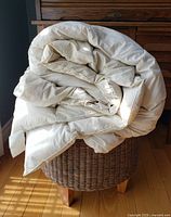 King size down duvet folded and placed on a woven basket seat, showing thickness and fabric quality.