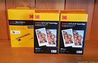 Photo showing Kodak Mini 2 Retro printer box and two Kodak photo cartridges boxes, all yellow with Kodak branding.