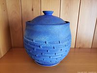 Large blue pottery cookie jar with lid in place shown against wooden panel background.