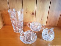 Full view of four lead crystal pieces: tall vase, sugar bowl, creamer, and candy bowl on wooden background