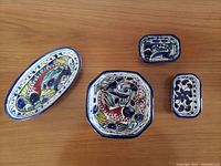 Top-down view showing all four handpainted Libyan pottery dishes with distinct colorful designs on a wooden surface.