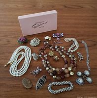 Full overview of all pieces laid out on wooden surface showing variety of necklaces, brooches, earrings, and pins including pearl strands, floral porcelain brooch, bronze brooch, and rhinestone items.