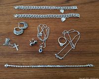 Full lot with 13 silverplate jewelry pieces including necklaces, bracelets, rings, earrings, and a cross pendant arranged on wooden surface