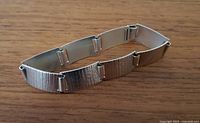 Top and side view of the silver bracelet laid on wooden surface showing textured linked segments.