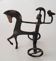 Side profile view of metal sculpture showing Etruscan horse with raised leg, female figure with helmet and owl on arm, and circular chariot wheels at base