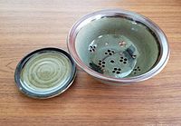 Two-piece pottery colander set shown on wooden surface, including bowl and matching plate base.