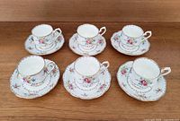 Top view showing six Royal Albert Petit Point teacups placed on matching saucers on wooden table.