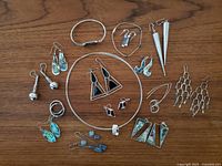 Full spread of sterling silver jewelry including earrings, bracelets, rings, and necklaces with garnet, onyx, and paua inlays, arranged on wooden surface.