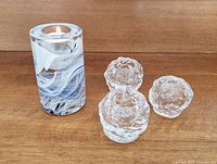 Photo showing one lit Kosta Boda glass candle holder in blue and white swirl pattern alongside three vintage clear textured snowball candle holders.