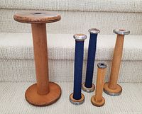 Five wooden textile mill bobbins styled as candlesticks with two wrapped in navy wool, arranged on beige carpeted steps.
