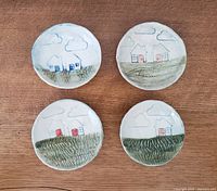 Top view of four small pottery dishes, each with unique painted house and landscape scenes featuring pastel colors and glazed finish