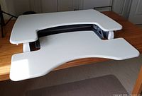 Top view of white sit-stand desk top with ergonomic cut-out and keyboard tray, placed on wood table.