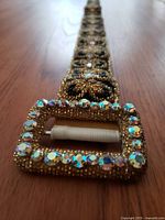 Close-up of the rectangular buckle covered with iridescent rhinestones and gold beadwork.