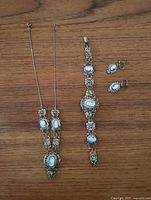 Full view of the three-piece jewelry set on wood surface: necklace, bracelet, and screw-on earrings all with filigree and cameo style inlays