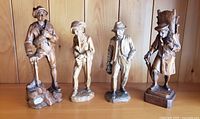Front view of four distinct wood carvings of men in traditional German attire shown together on a wooden surface.