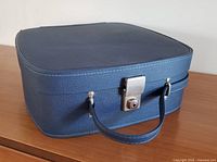 Side angle view of blue vintage hand luggage case showing silver-tone clasp lock and handle.