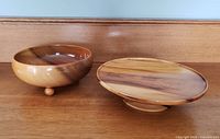 Image showing side by side views of the two vintage myrtlewood pieces; fruit bowl on left with three small feet and round cake stand on right with pedestal base.