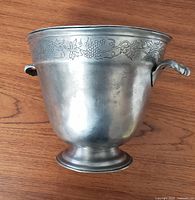 Front view of the pewter champagne bucket showing the grapevine engraving and one handle.