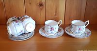 Six Royal Albert petite point pattern teacups and matching saucers displayed on a wood surface. Two teacups placed on saucers to show design and set detail while the rest are stacked.