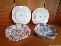 Front and back view of two stacks of eight Royal Albert Petit Point sandwich plates, showing four smaller and four larger plates with floral and zig-zag design, gold trim. Backstamp with Royal Albert logo visible.
