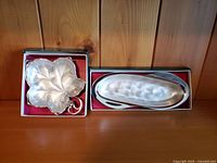 Two silverplate WMF Ikora trinket dishes in original boxes on wooden background, one leaf-shaped and one elongated oval shaped with hammered texture.