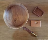 Photo showing the four wooden items arranged together: macrocarpa bowl, myrtlewood letter opener, kauri business card case, and rimu business card holder on a wooden surface.