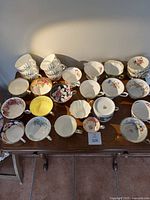 Wide view showing 27 different porcelain cups arranged on a wooden table, displaying varied floral and gold-accented designs.
