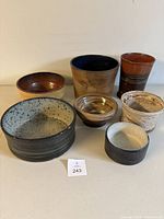 Photo showing all seven handcrafted pottery pieces arranged in two rows on a white surface, showcasing varying sizes, shapes, and colors.