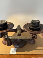 Front view of antique cast iron Burrows Stewart Milne scale showing two weighing pans and cast iron weights placed on pans.