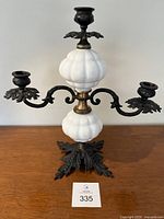 Full view of antique cast iron, brass and milk glass candelabra showing three candle holders and detailed base.