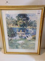 Framed print showing the impressionistic artwork with a girl in a boat on a lake surrounded by trees in a gold frame.