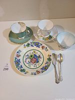 Top view of five china pieces and two silver spoons arranged on table