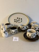 Full view of all 13 pieces in the Denby Shamrock dishware set arranged with cups on saucers, platters, and shakers visible.