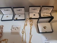 Jewelry items displayed including earrings in boxes, men’s tie pins in boxes, and gold-tone necklaces and bracelets laid out
