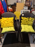 Pair of two dark brown faux wicker chairs with lime green seat cushions and raised yellow petal-textured throw pillows, shown side by side indoors.