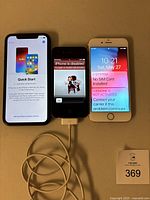 Three Apple iPhones side by side on table: one on setup screen, one disabled, one with SIM card error. White charger cable connected to center phone.