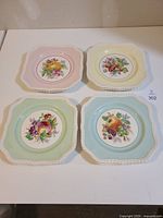 Four vintage luncheon plates by Johnson Bros arranged in a square showing different pastel colored borders and central fruit motifs.